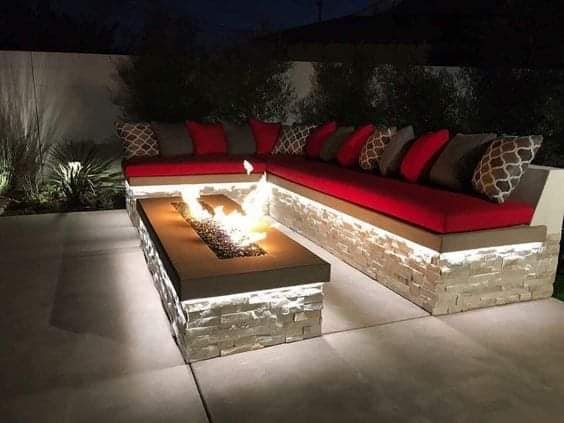 Custom built-in fire pit lounge with stone seating, lit at night